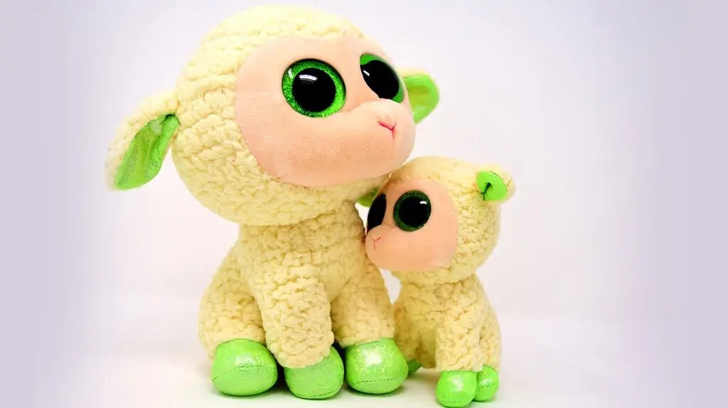 Two yellow plush lamb toys with large green eyes and shiny green feet sitting together on a white background.