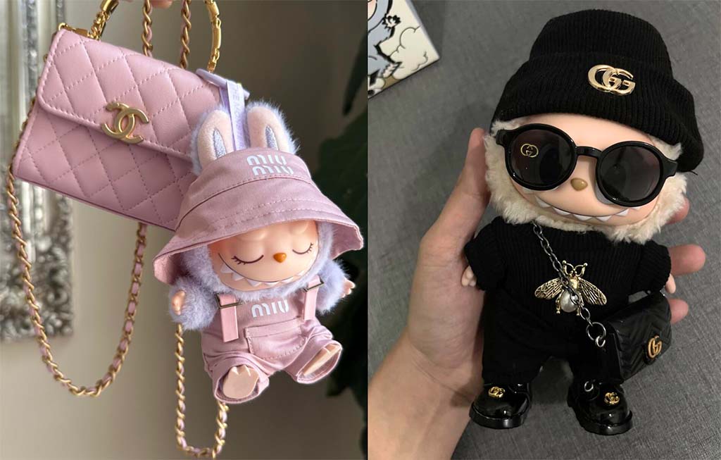 Two Labubu dolls dressed in luxury-inspired outfits — one in pink Miu Miu attire beside a Chanel bag, and another in black Gucci-style clothing with sunglasses and gold accessories.