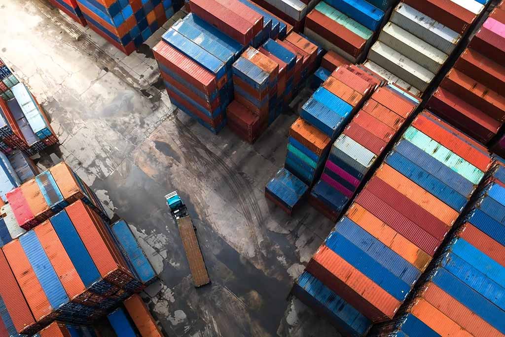 An aerial view of stacked colorful shipping containers with a truck moving through the loading area at a port.