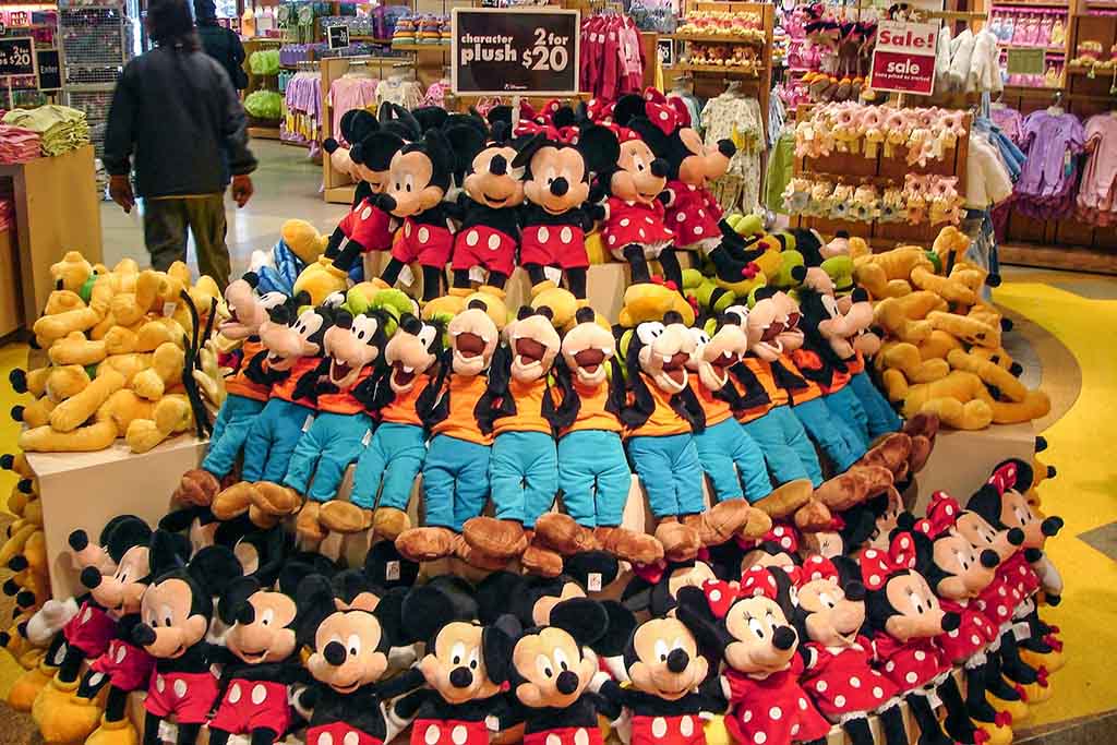 Display of Disney plush toys featuring Mickey Mouse, Minnie Mouse, Goofy, and Pluto arranged in tiers inside a retail store.