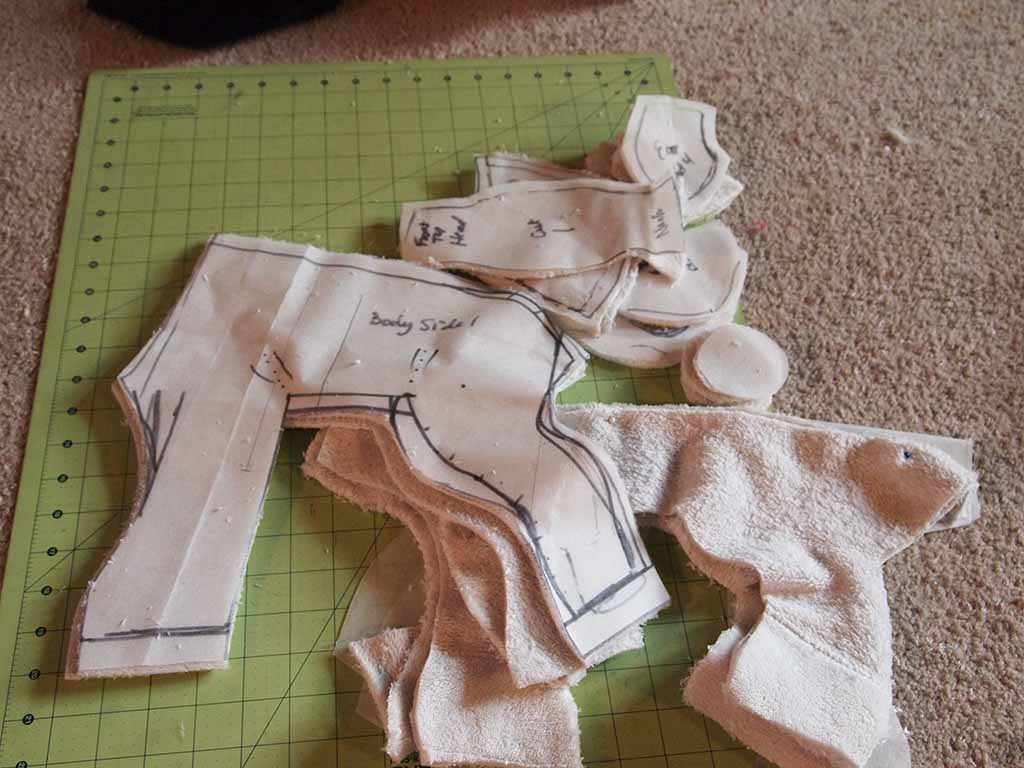Fabric pieces with traced plush toy sewing patterns laid out on a green cutting mat and carpet, showing various parts ready for assembly.