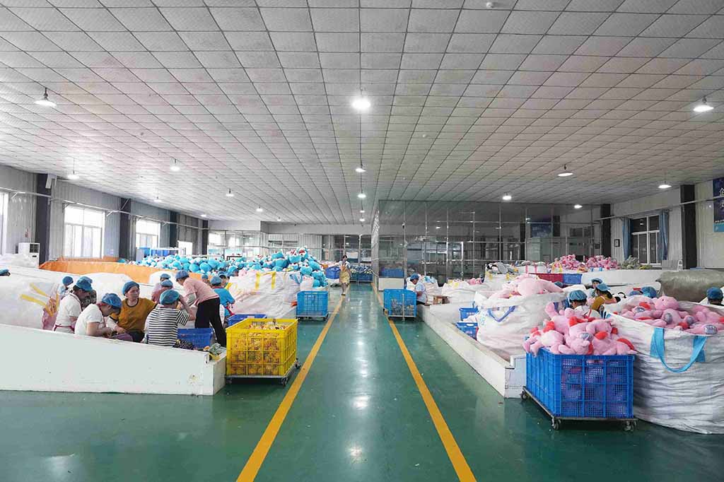 Workers in a plush toy manufacturing factory sorting and packaging stuffed animals in large batches, with blue and pink plush toys organized in bins.