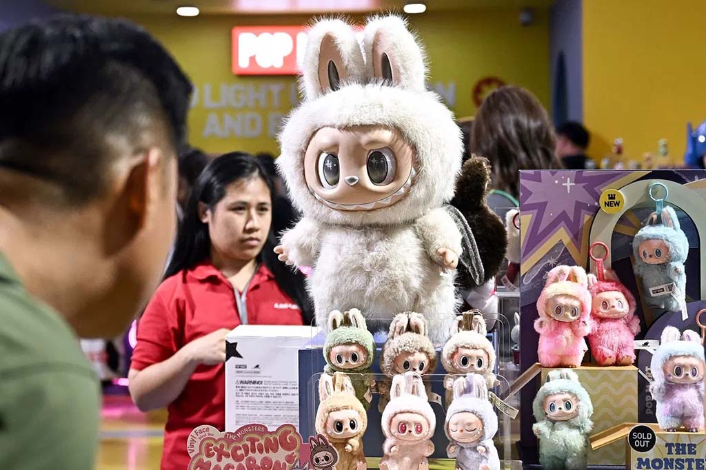 Large and mini Labubu plush figures displayed at a Pop Mart store counter, with shoppers and staff in the background viewing the collectible toy collection.