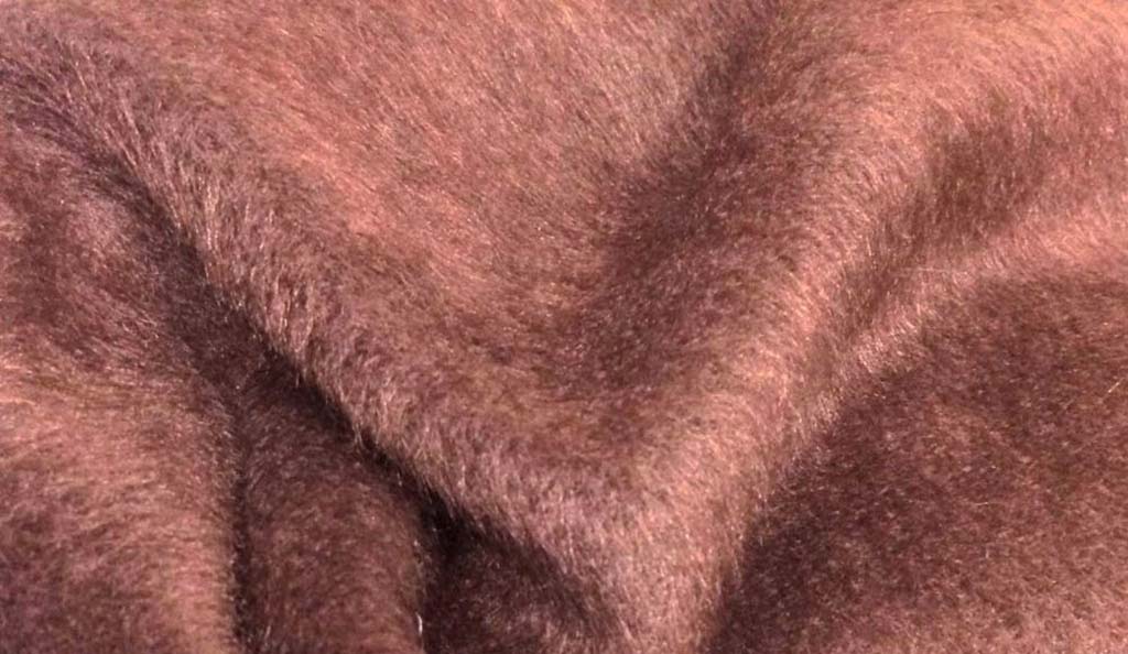 Close-up view of soft short-pile brown plush fabric showing its smooth texture and dense fibers, commonly used in plush toys and teddy bear manufacturing.