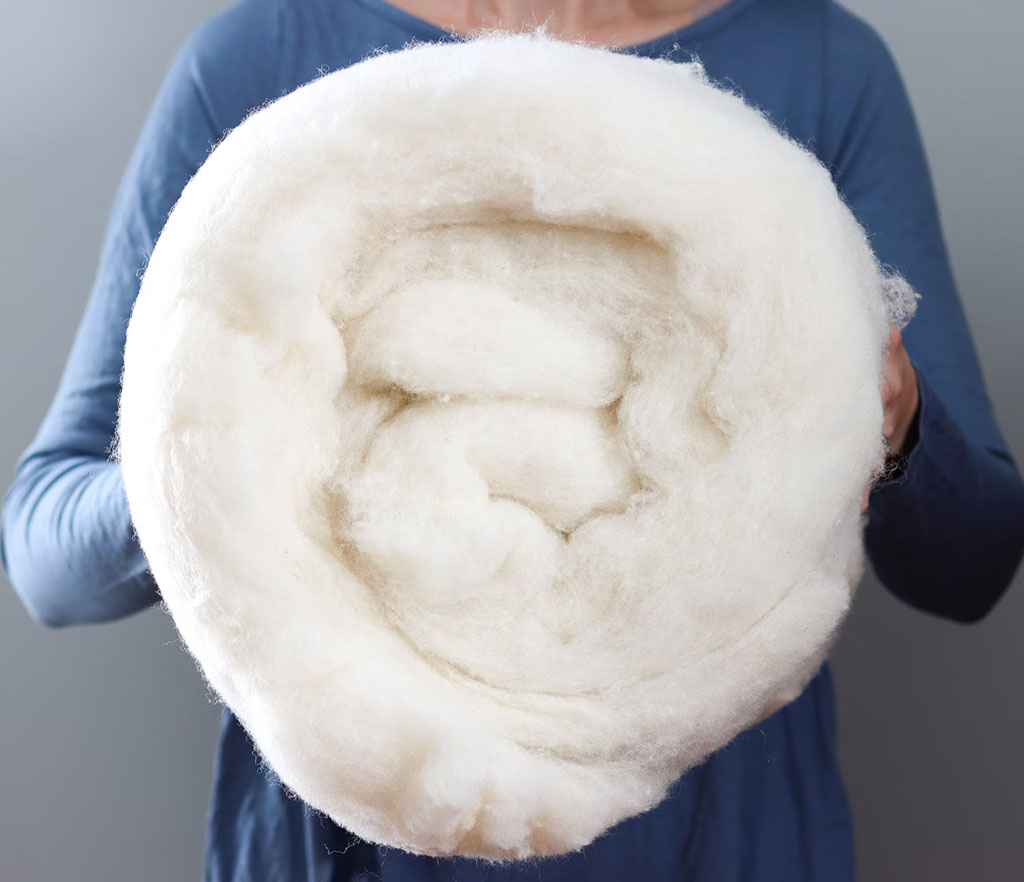 A person holding a large rolled bundle of soft natural wool batting used for stuffing or padding.