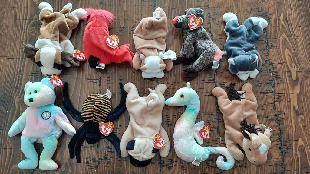 Assorted TY brand plush toys arranged on a wooden surface, including bears, dogs, a spider, a seahorse, and other animal characters.