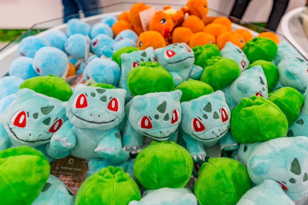 Pile of Bulbasaur plush toys with bright red eyes and green bulb backs, displayed together in a store bin.