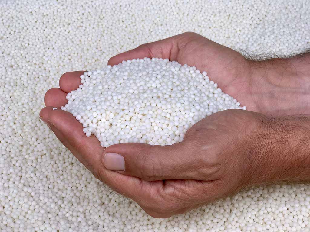 Hands holding white expanded polystyrene (EPS) beads used as lightweight filling material for plush toys and cushions.