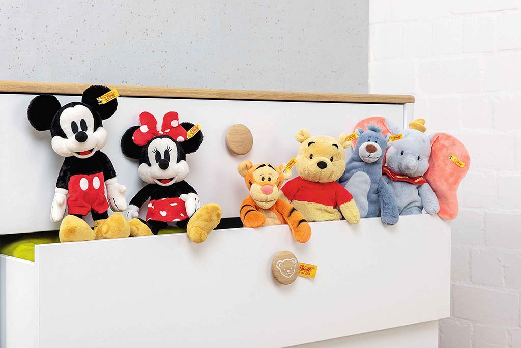 Soft plush toys of Mickey Mouse, Minnie Mouse, Tigger, Winnie the Pooh, Baloo, and Dumbo sitting on a white dresser in a cozy children’s room.