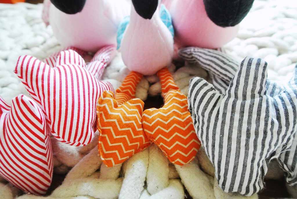 Assorted striped and chevron-patterned fabric pieces in red, orange, and black, arranged around a soft plush toy on a knitted surface.