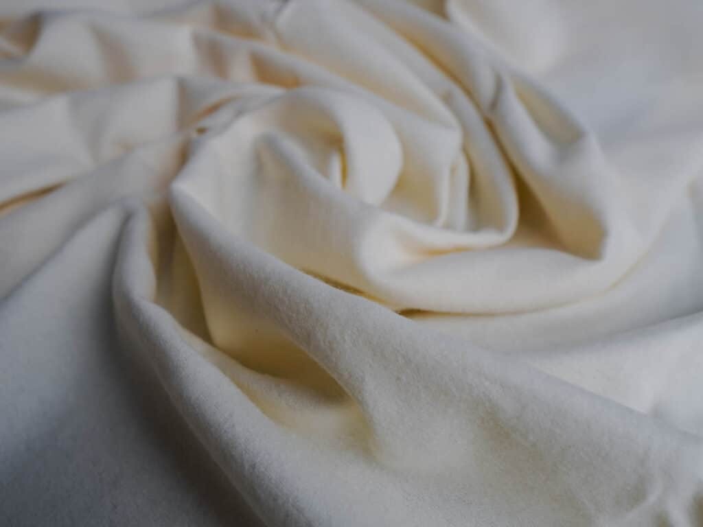 Close-up of soft cream-colored brushed cotton fabric with gentle folds, showing its smooth texture and plush feel, commonly used for premium plush toys and baby products.
