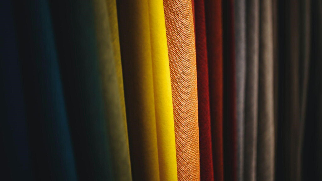 Close-up of vertically hanging fabric rolls in assorted colors, ranging from dark blues to bright yellow and warm red tones.