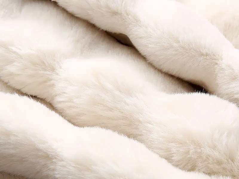 Close-up of creamy white faux fur fabric showing its dense, silky, and smooth pile texture.