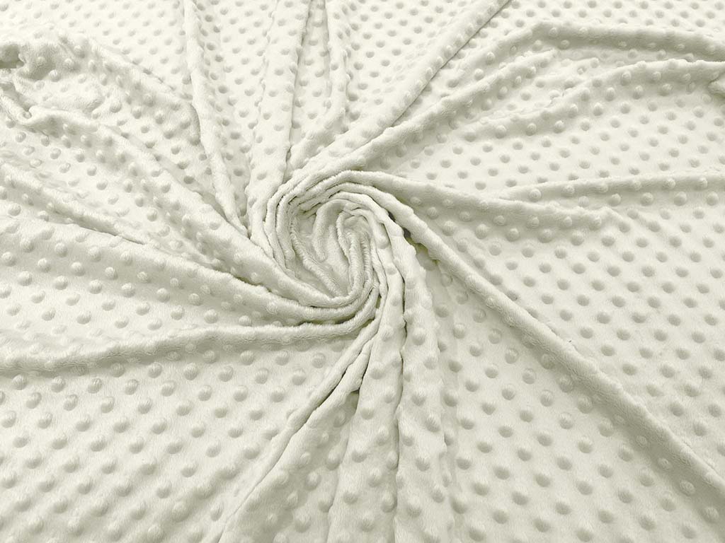 Close-up of soft white dimple minky fabric laid out in a spiral pattern, showing its raised dot texture and plush surface.