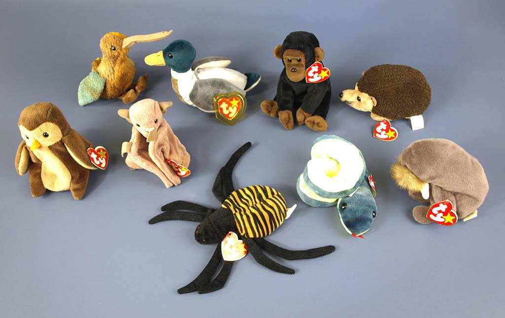 Assorted Ty Beanie Babies animal plush toys arranged on a blue surface, including bird, monkey, snake, spider, and hedgehog characters.