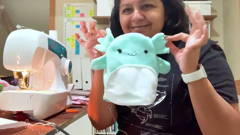 Smiling person holding a mint-green handmade plush toy near a sewing machine, showing a cute finished craft project.