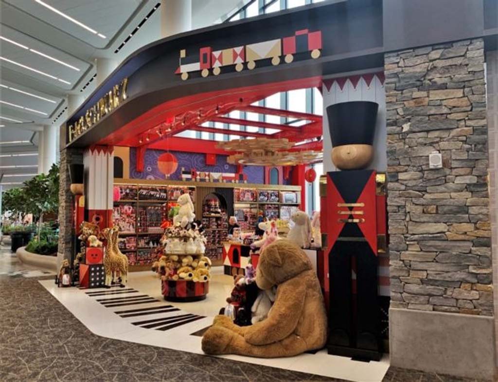 Colorful FAO Schwarz toy store entrance featuring a large toy soldier figure, plush animals, bright red décor, and displays filled with stuffed toys inside a modern shopping area.