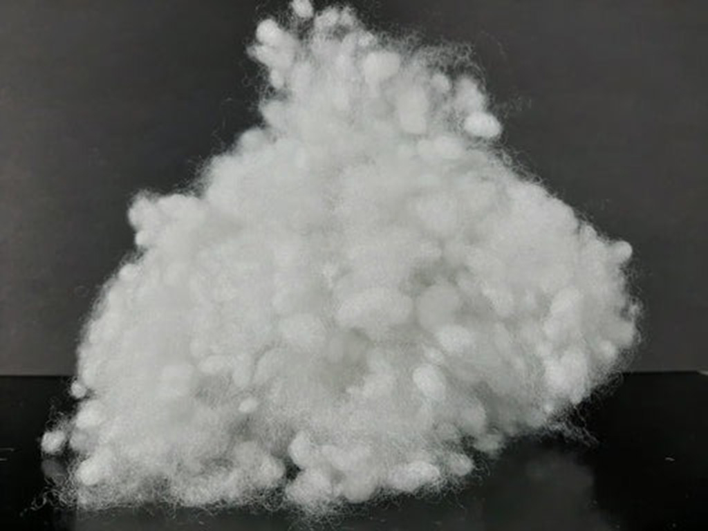Soft white polyester fiberfill shown in a fluffy pile against a dark background, highlighting lightweight, durable stuffing used in plush toys.