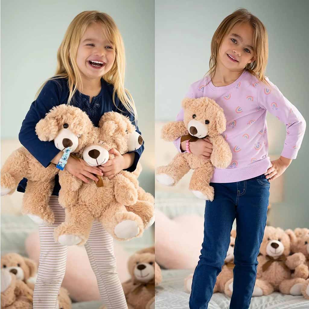 Two young girls happily holding soft beige teddy bears, smiling and posing indoors with more plush toys in the background.