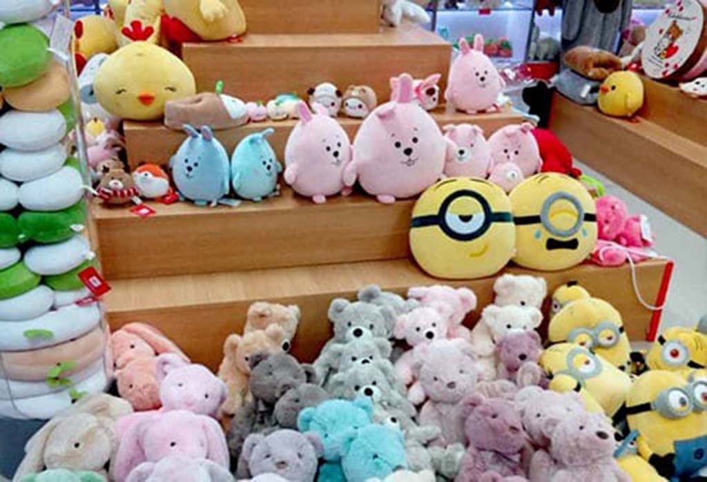 Colorful display of custom plush toys including bears, bunnies, and cartoon characters arranged on wooden shelves in a retail store.