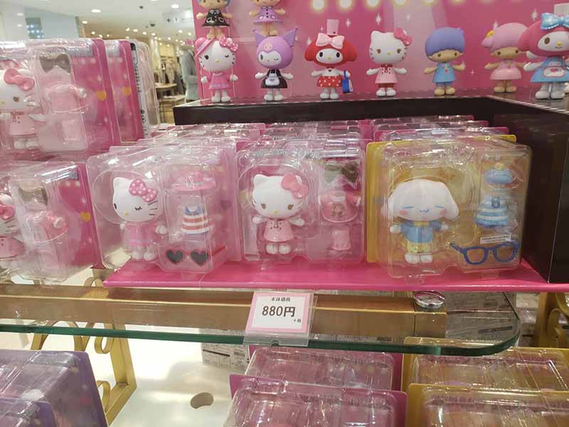 Hello Kitty and Sanrio character collectible figures packaged in clear plastic boxes on a store shelf with a price tag of 880 yen.