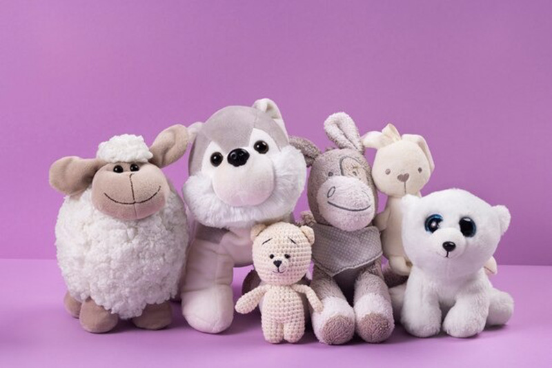 A group of neutral-colored plush toys, including a sheep, husky, teddy bear, donkey, rabbit, and white polar bear, arranged against a purple background.