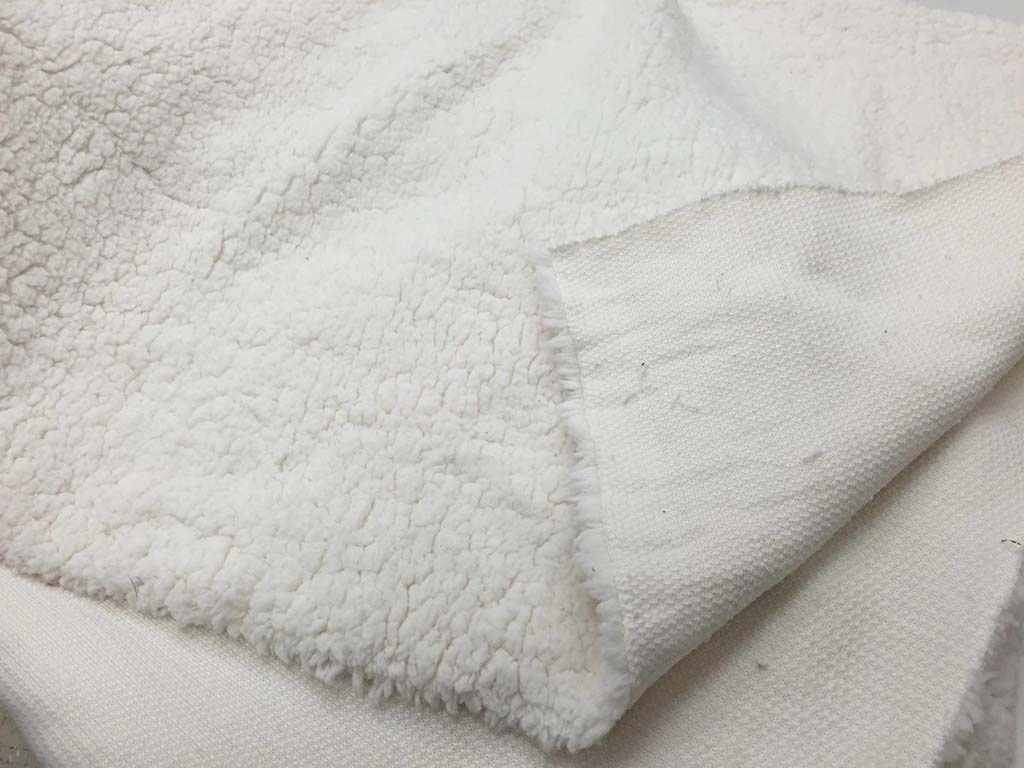  Close-up of soft white sherpa fabric showing its fluffy fleece surface and sturdy woven backing, commonly used for plush toys, blankets, and cozy apparel.