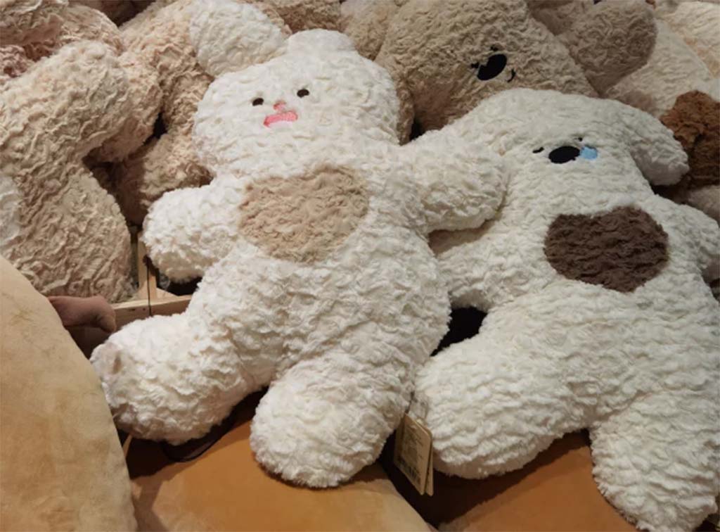 Close-up of soft, curly-textured plush toys in bear and bunny shapes with heart patterns, showing cozy and fluffy fabric detail.