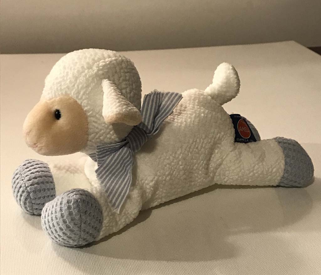 White plush lamb toy lying down with a striped bow, textured grey paws, and soft fleece fabric, designed for babies and children.