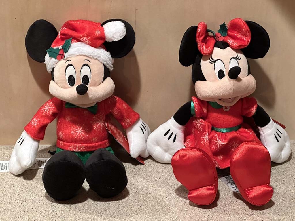 Mickey Mouse and Minnie Mouse Christmas plush toys wearing red holiday outfits, sitting side by side on a beige surface.