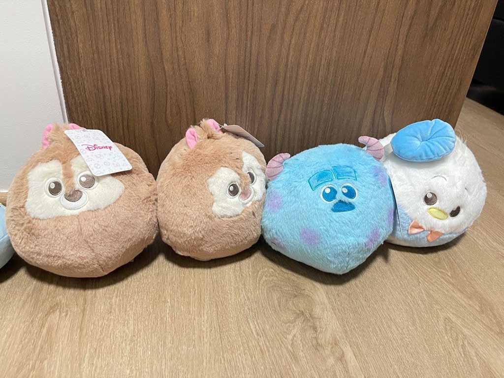 Four round Disney-themed plush toys, including two chipmunk characters, a blue monster, and a white duck, arranged side by side on a wooden floor.