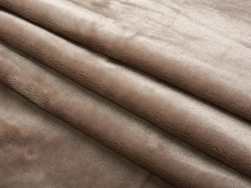 Close-up view of folded brown plush fabric with a smooth, short-pile texture used for stuffed animals and soft toys.