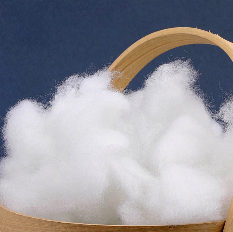 Fluffy white polyester fiberfill used as plush toy stuffing, displayed in a wooden container to show its softness, bounce, and high-loft quality.