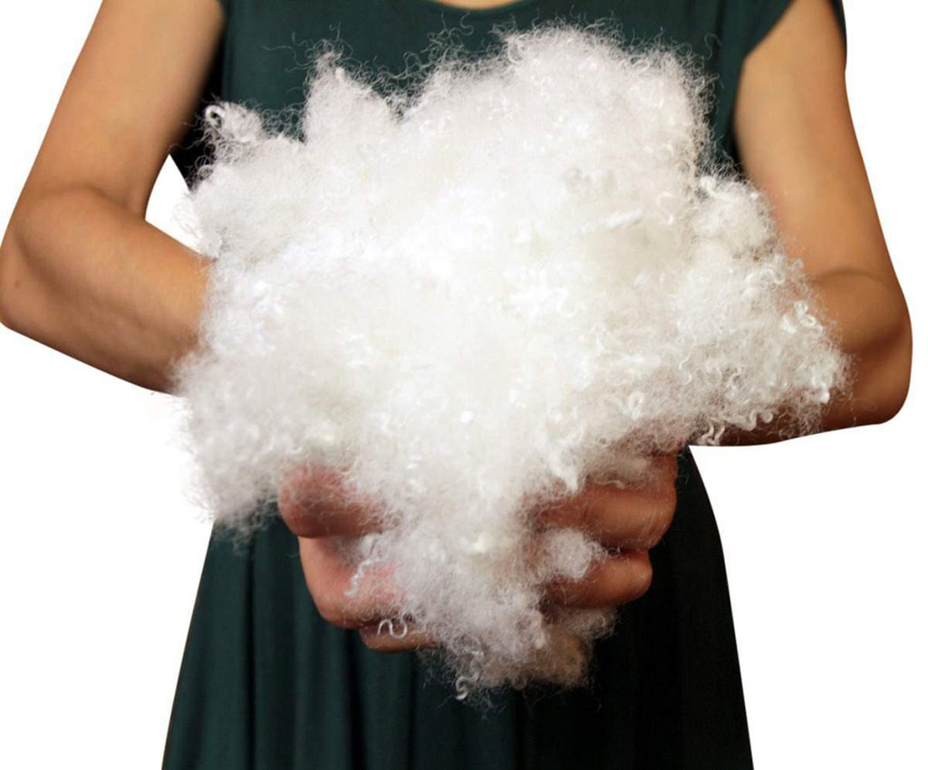 Person holding a large handful of soft white polyester fiberfill stuffing used for plush toys and cushions.