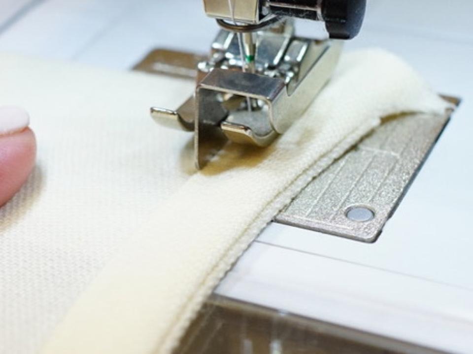 Close-up view of a sewing machine stitching fabric with a bias-binding attachment.