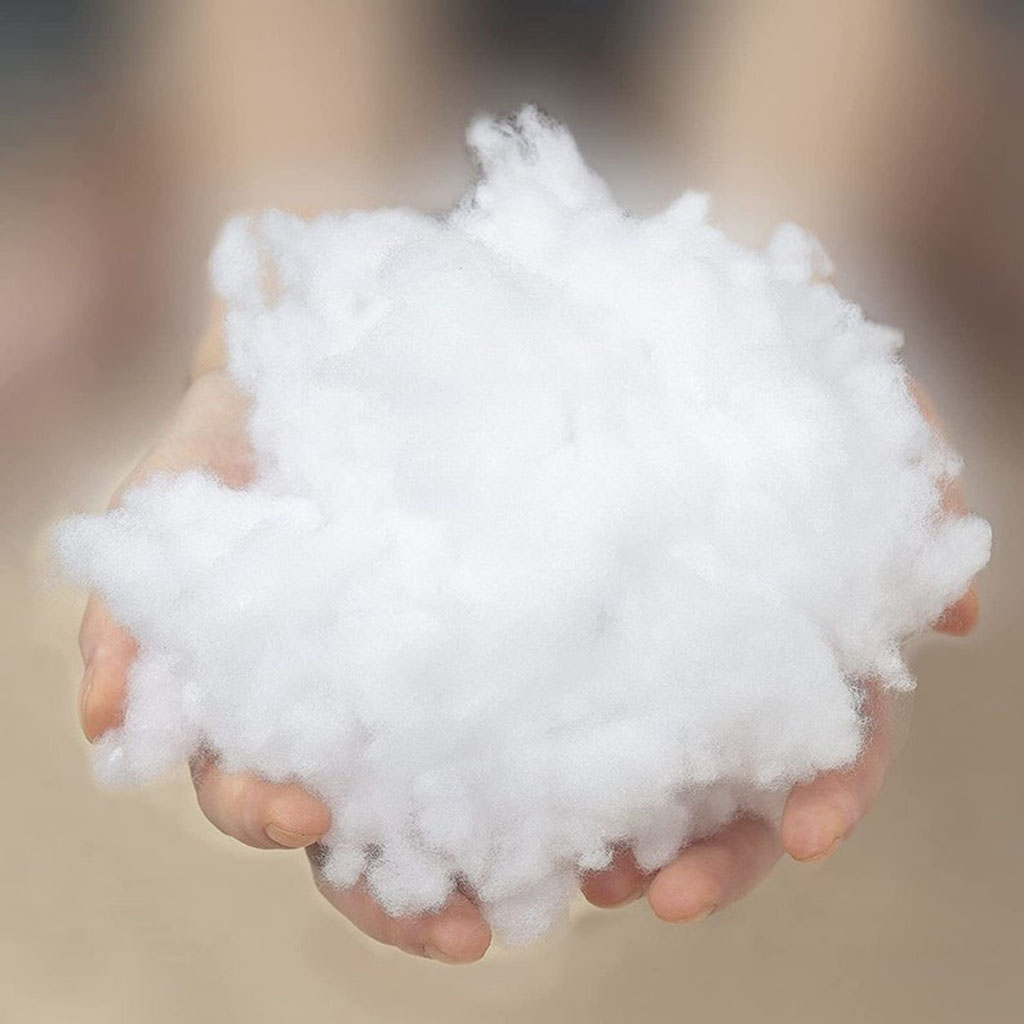 Hands holding a large bundle of soft white polyester fiberfill stuffing, commonly used inside plush toys, pillows, cushions, and handmade crafts.