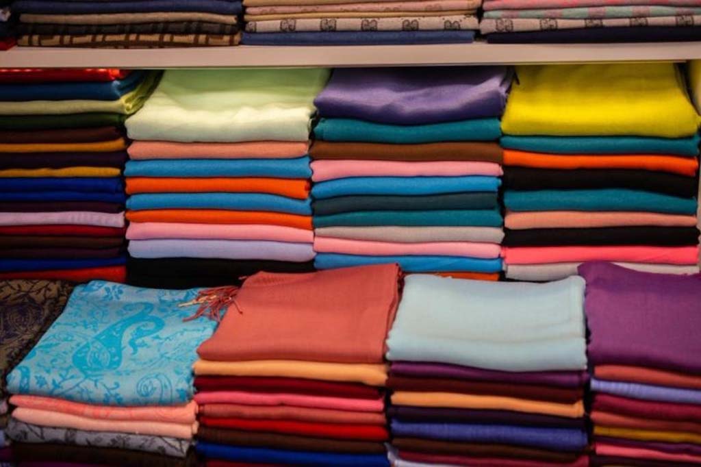 Neatly stacked piles of multicolored fabric in various textures and materials, displayed on shelves to show color options for textile or plush toy production.