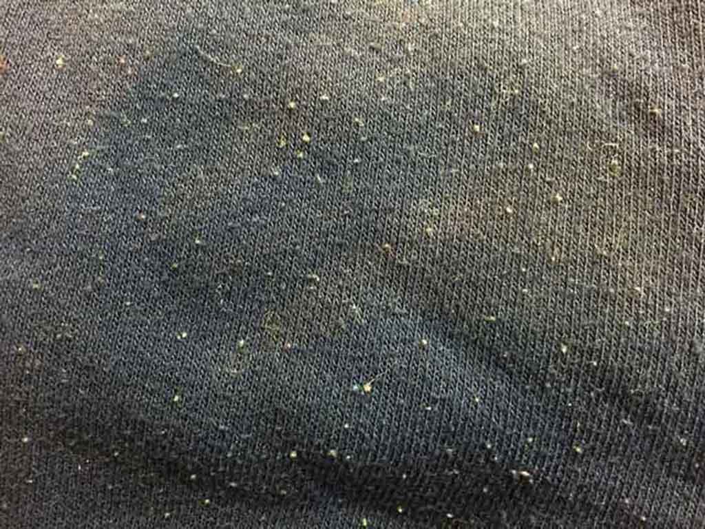 Close-up view of dark fabric showing pilling and tiny lint balls on the surface.