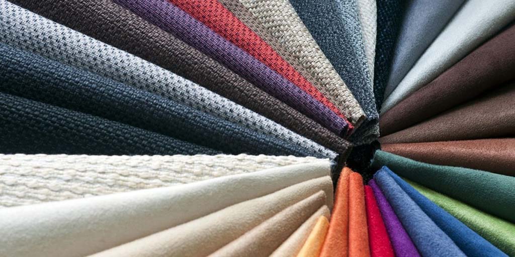 A circular display of assorted fabric swatches arranged like a fan, showing a wide range of colors and textures from neutrals to vibrant shades, commonly used for selecting materials in plush toy and textile production.