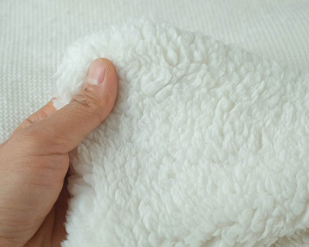 Hand holding a piece of soft white sherpa plush fabric, showing its fluffy and cozy texture ideal for stuffed animals and baby products.