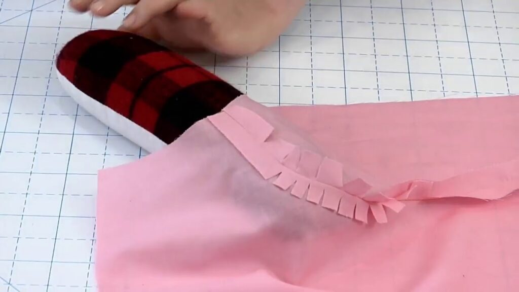 Close-up of pink fabric seam allowance being clipped into small notches and pressed open with a tailor’s ham to help curve lie flat during sewing.