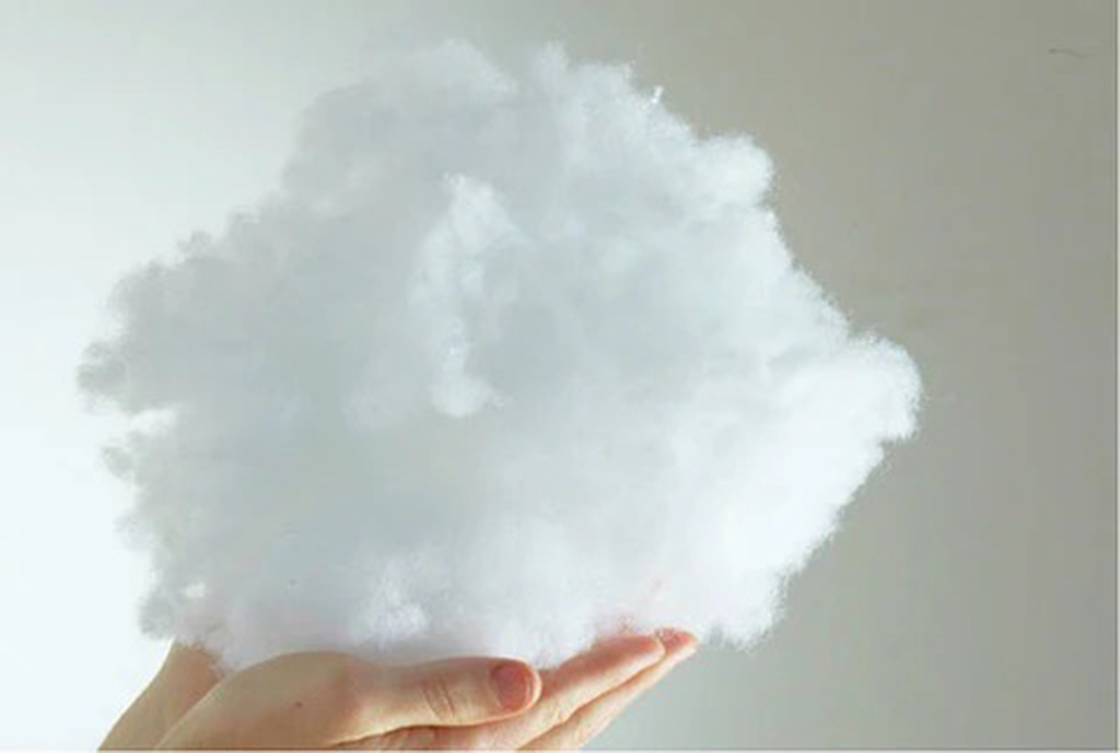 A hand holding a large fluffy bundle of white polyester fiberfill stuffing against a plain background.