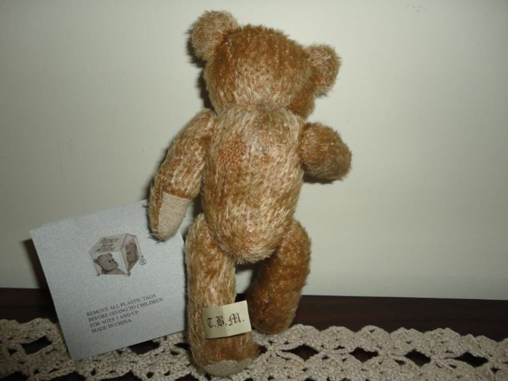 Two classic teddy bears sitting on a wooden surface, one wearing a lace collar and the other with a red plaid ribbon, representing early handmade teddy bear styles.