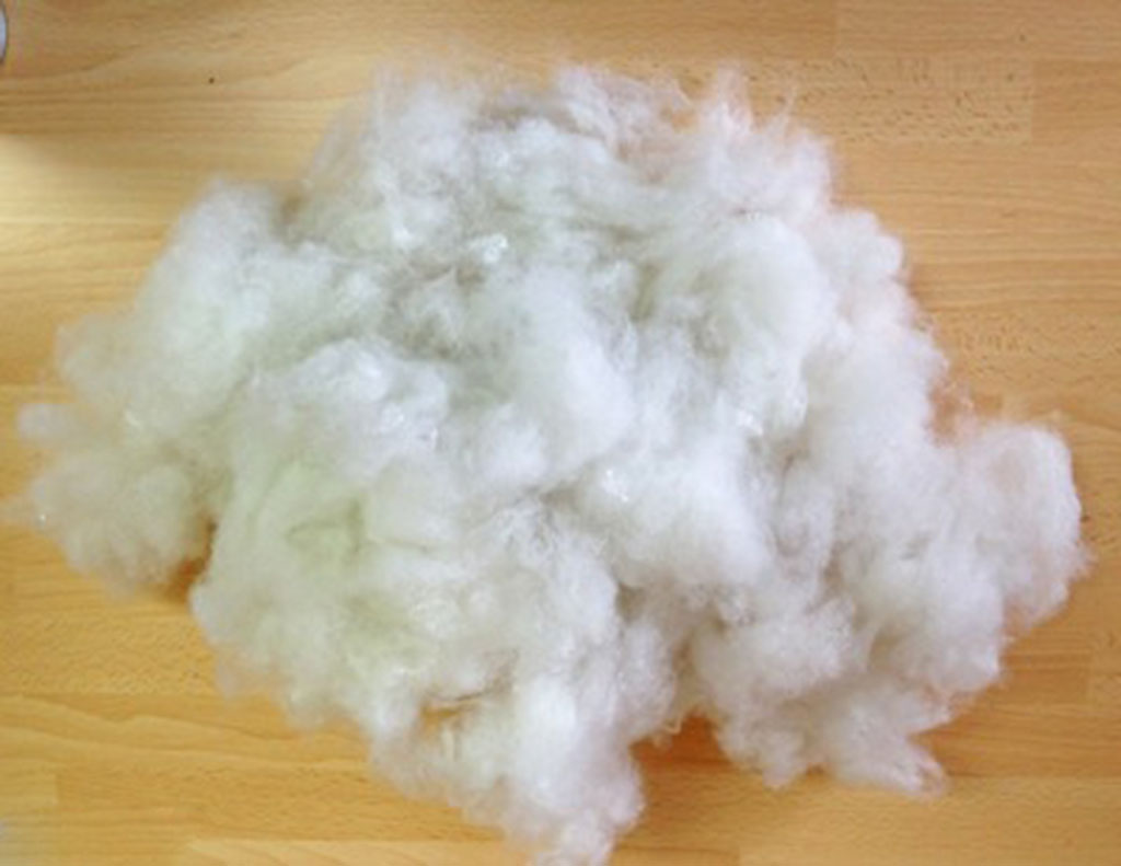 Fluffy white polyester fiberfill pile on a wooden surface used for stuffing plush toys and cushions.