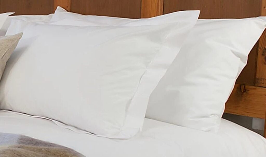 Two white pillows in smooth cotton pillowcases arranged neatly against a wooden headboard on a freshly made bed.