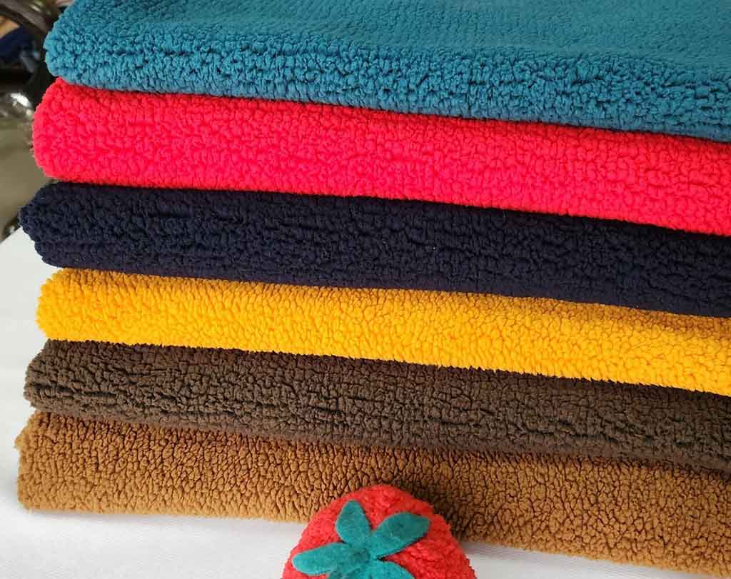 Pile of colorful sherpa fabrics in teal, red, navy, yellow, and brown tones, showcasing soft, textured fleece material ideal for plush toys and cozy products.