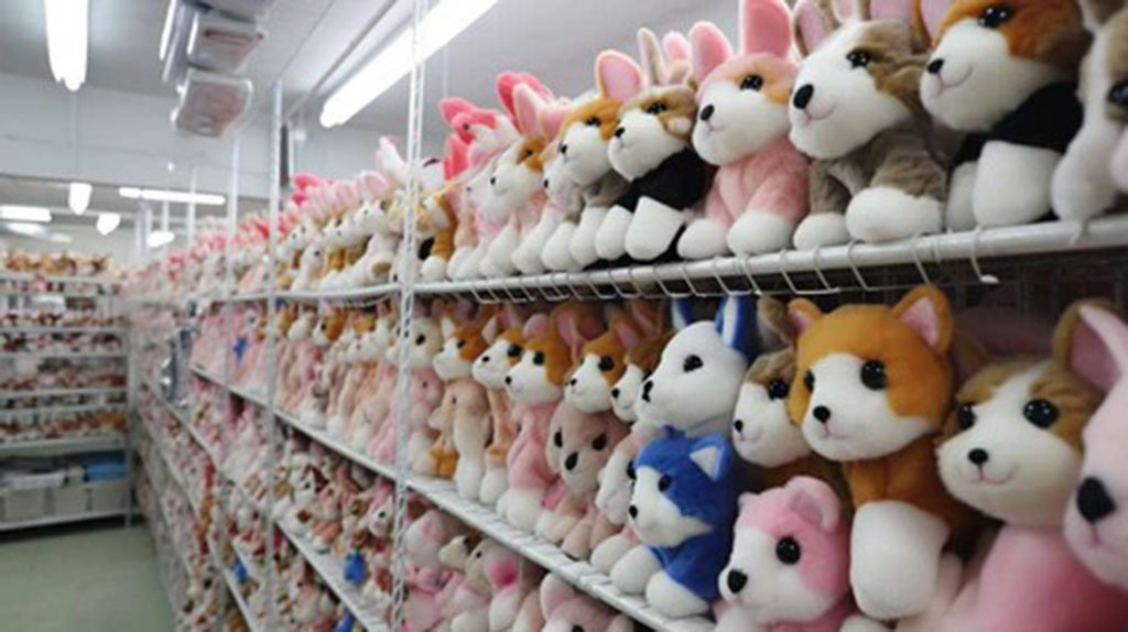 Rows of plush dog and bunny stuffed animals neatly arranged on factory storage shelves, showing organized inventory inside a plush toy manufacturing facility.