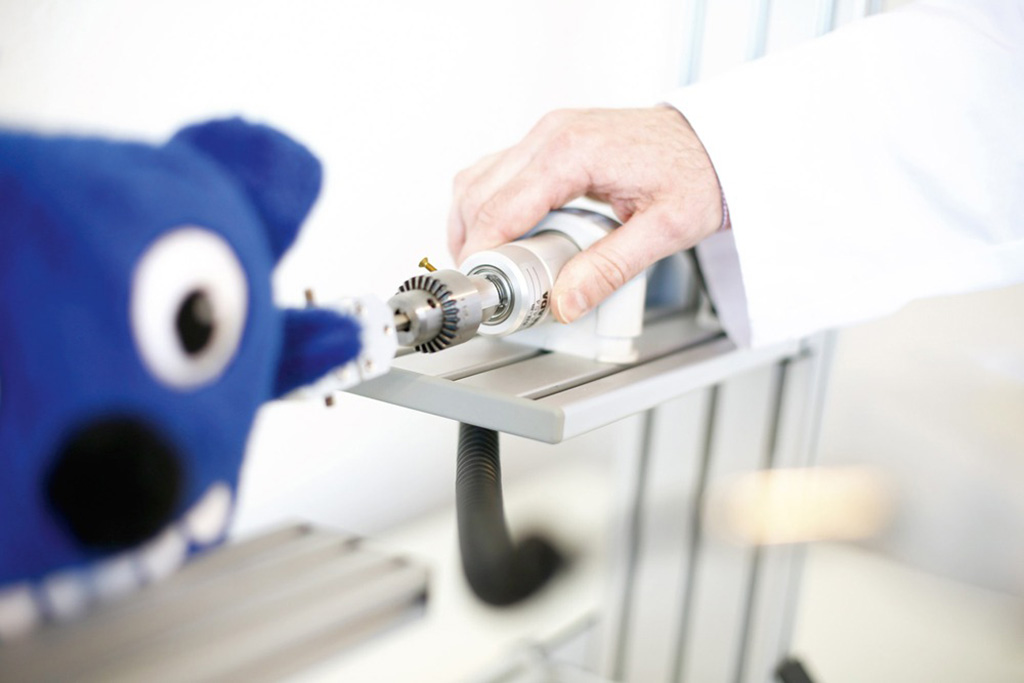 A technician using a mechanical testing device to check the durability and safety of a blue plush toy’s arm.
