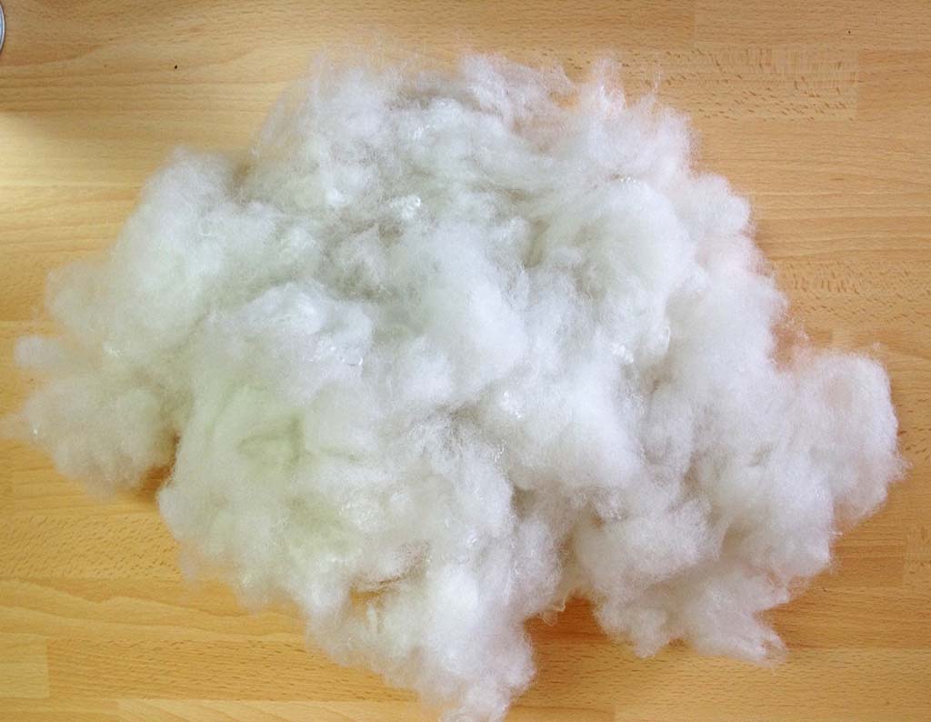 Soft white polyester fiberfill material spread on a wooden surface, commonly used as stuffing for plush toys and pillows.