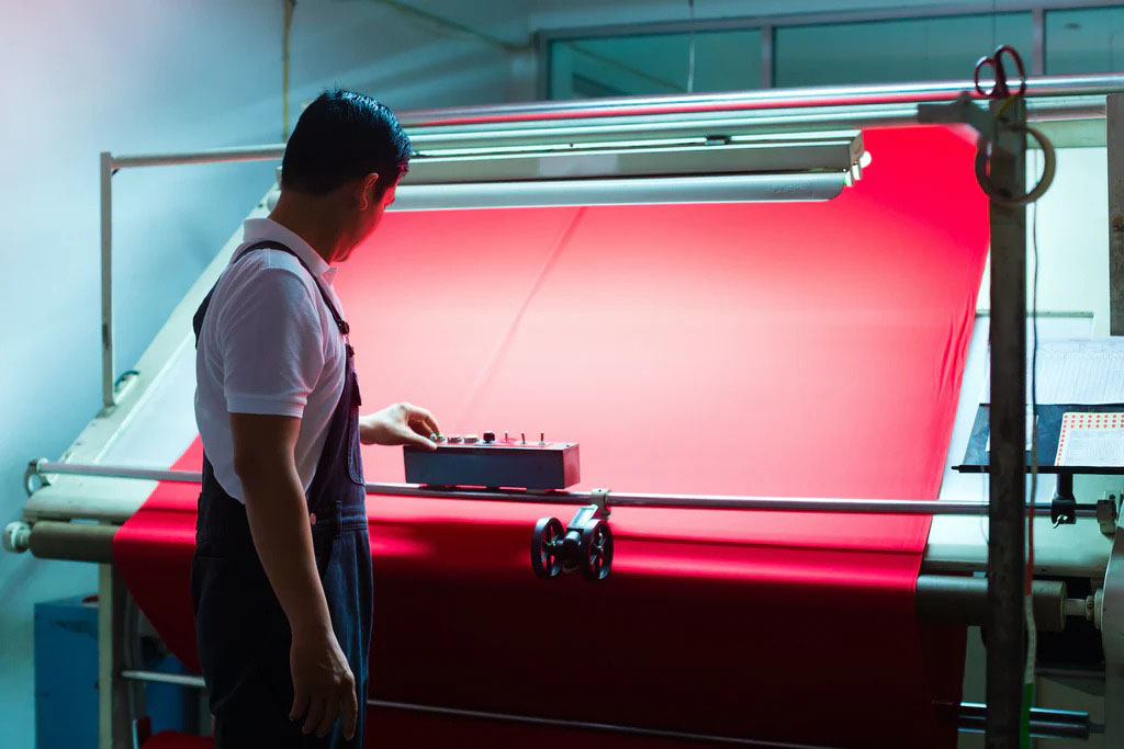 Technician inspecting bright red fabric on a textile production line under controlled lighting to ensure quality and consistency.